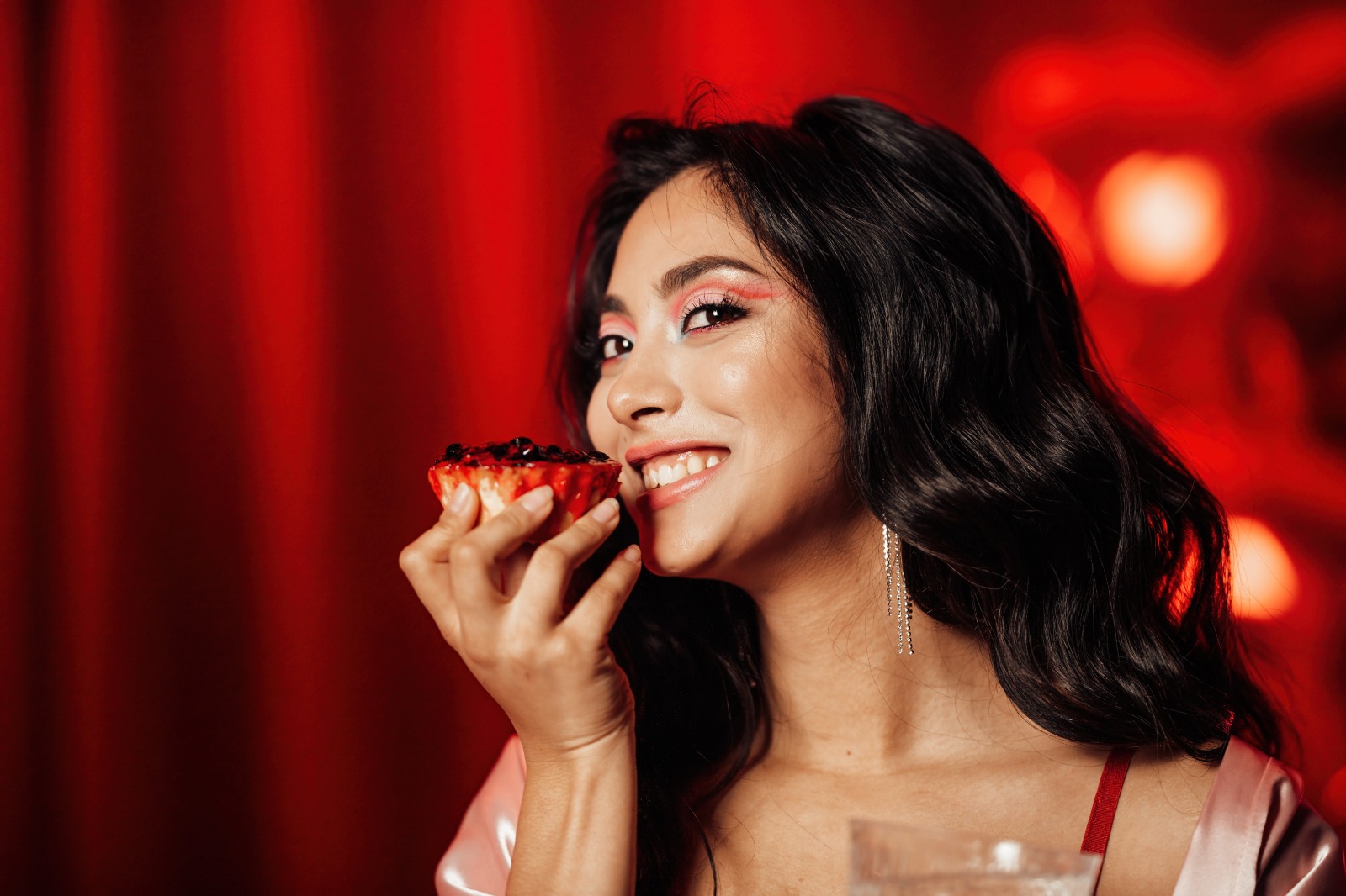 Woman smiling while holding a berry tart, against a rich red background