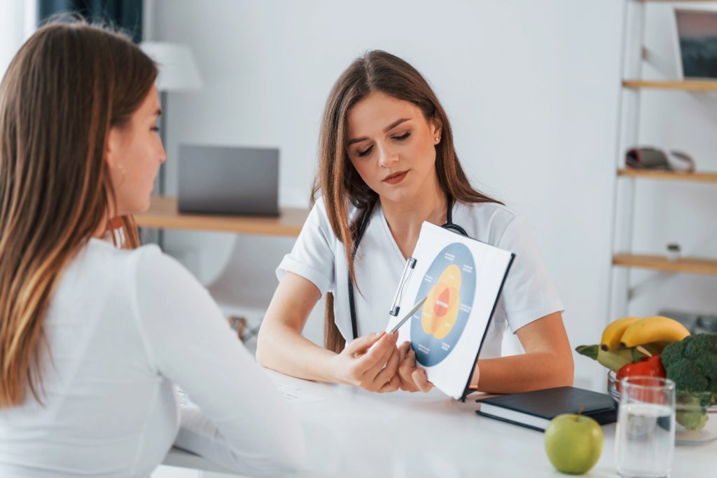 A female doctor discussing a detailed anatomical or hormonal chart with a woman during a clinical consultation.