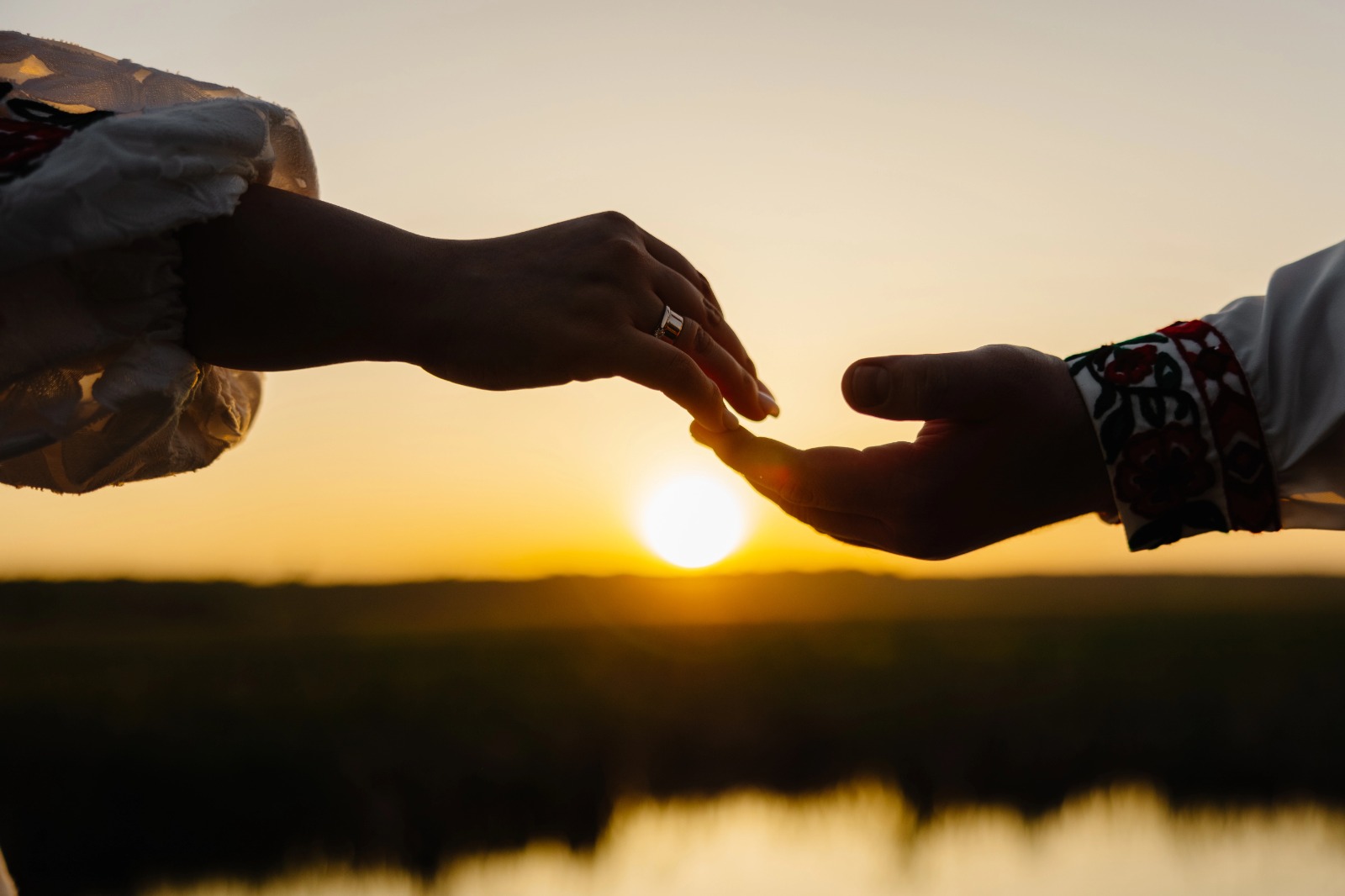 Silhouette of a couple gently holding hands against a sunset backdrop