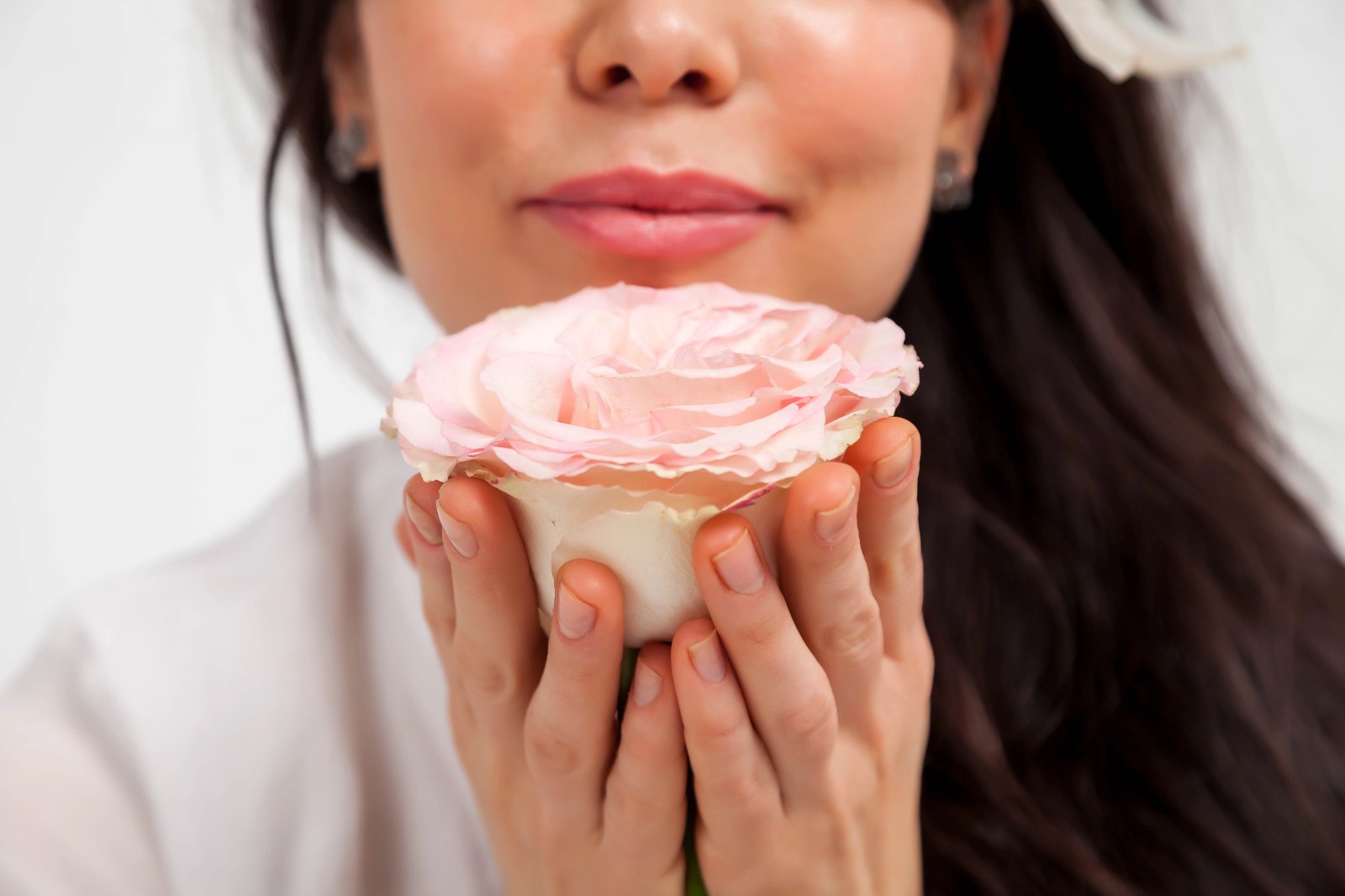 Close-up of a woman gently holding a soft pink rose near her face, symbolizing femininity and sensuality.