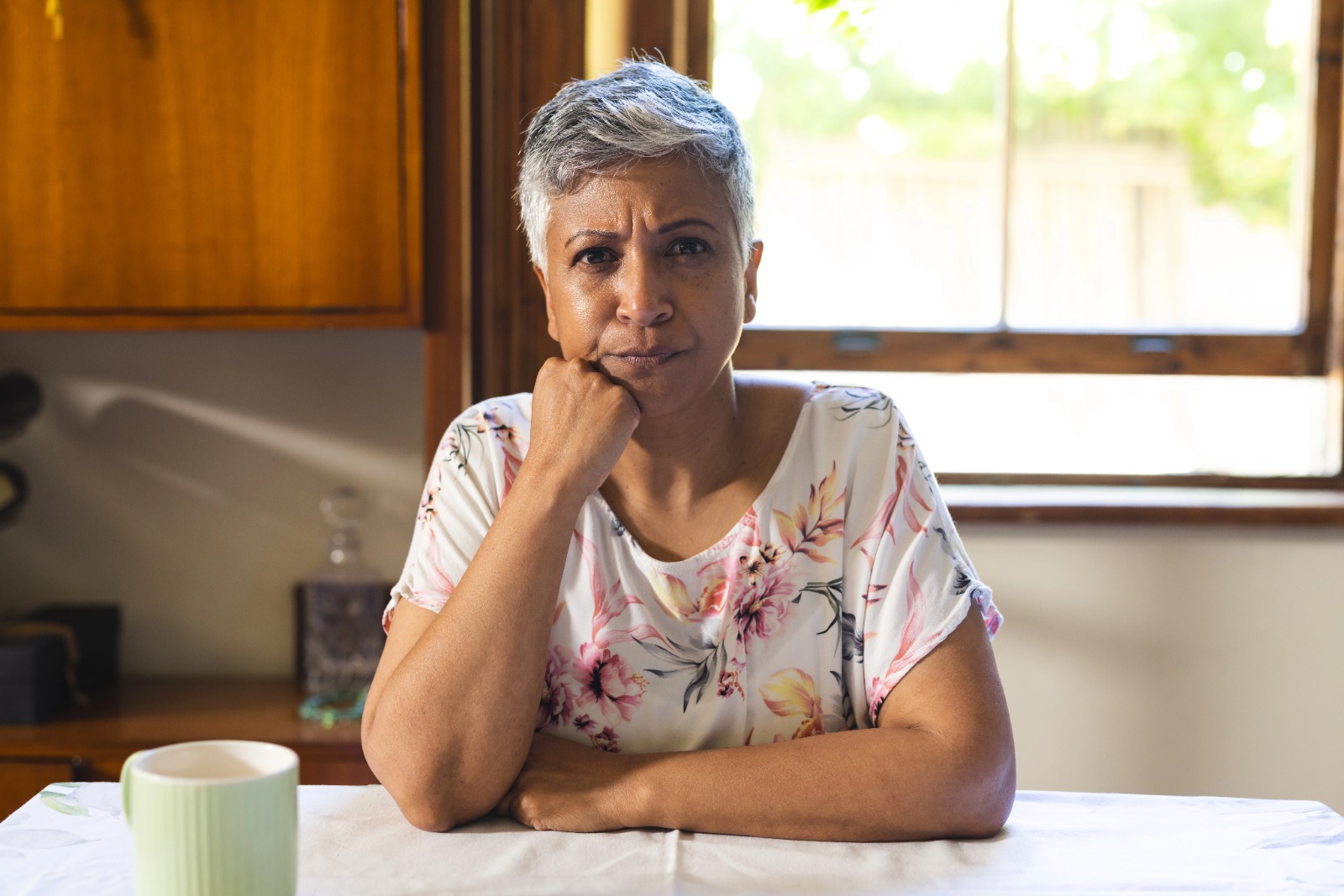 Midlife woman sitting thoughtfully at a table, reflecting on health, vitality, and female orgasm.