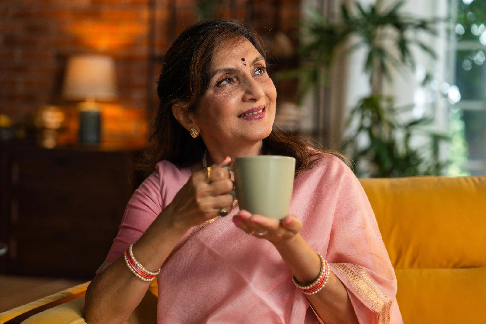 Elegant middle-aged Indian woman in a pink saree, smiling softly while holding a cup of tea, representing wellness and vitality with Miror Thrive.