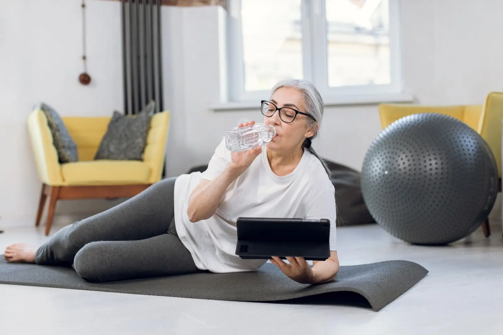 Older woman resting after yoga, hydrating with water — a Miror Thrive moment of postmenopausal wellness and self-care.
