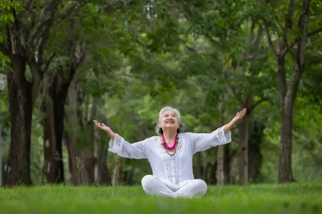 Senior woman practicing yoga in a green park, smiling with arms raised, symbolizing joint pain relief and vitality with MIROR MILY supplement.