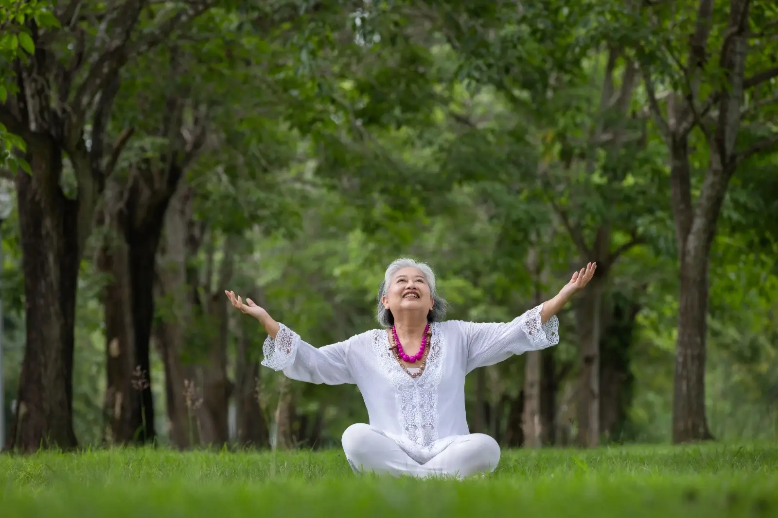 Senior woman practicing yoga in a green park, smiling with arms raised, symbolizing joint pain relief and vitality with MIROR MILY supplement.