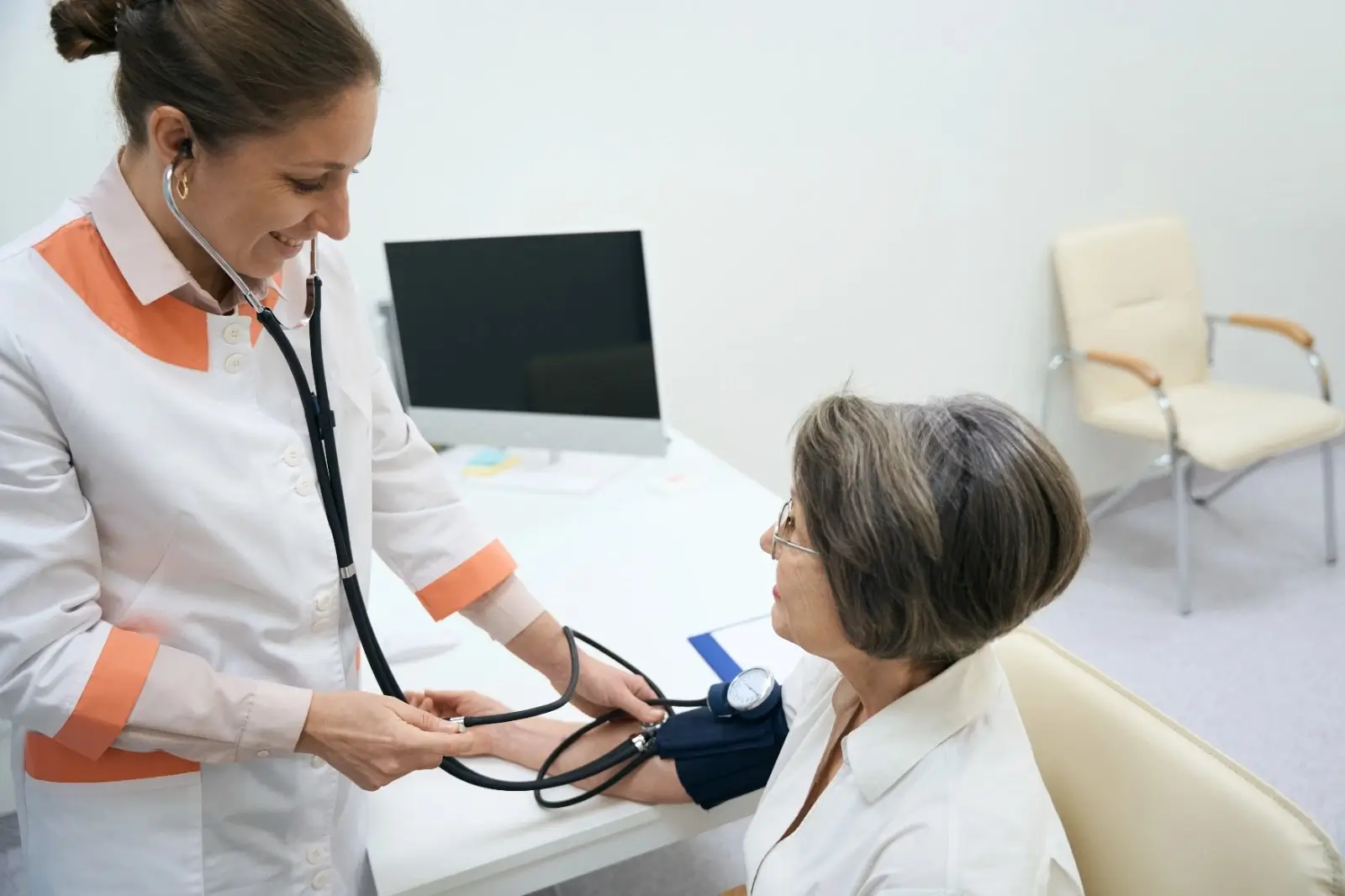 Female doctor checking blood pressure of an older woman during a routine health check-up in a clinical setting.