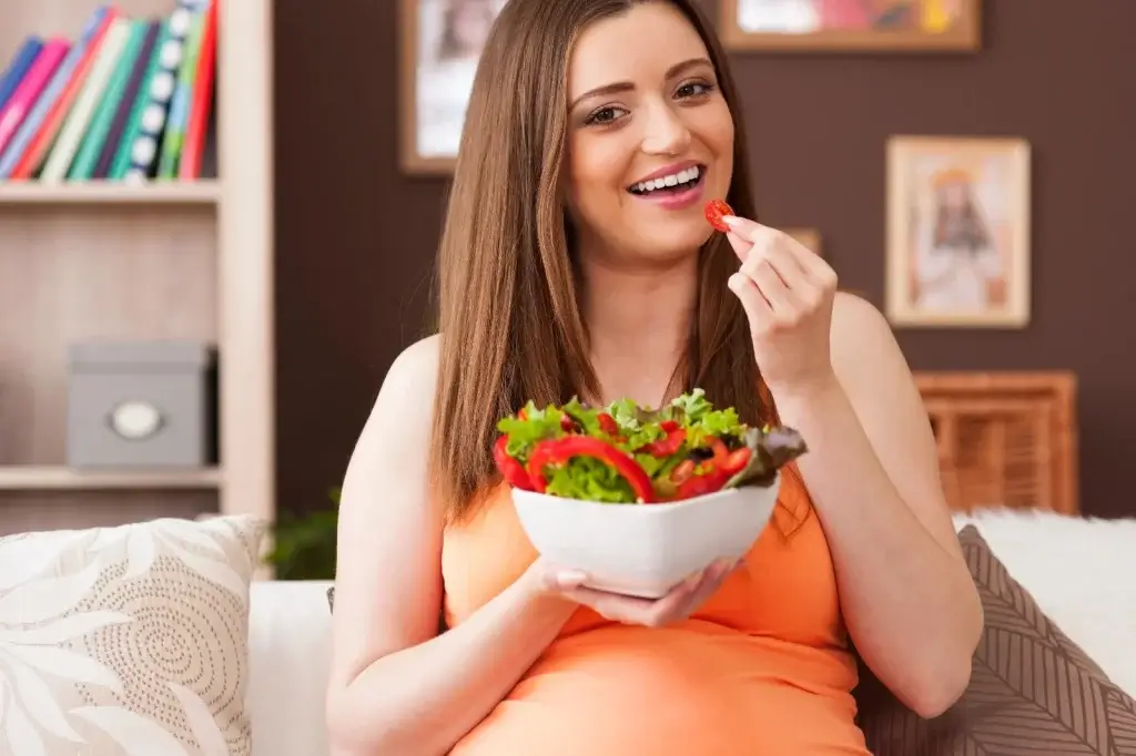 Happy pregnant woman eating fresh salad for fertility and reproductive health.