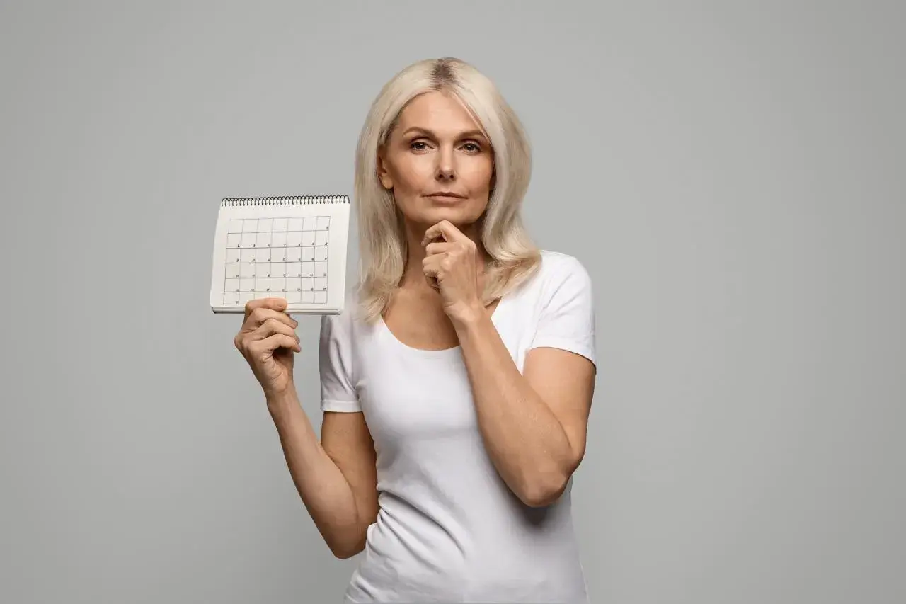 Pensive mature woman holding blank menstrual calendar, thinking about menopause and irregular periods.