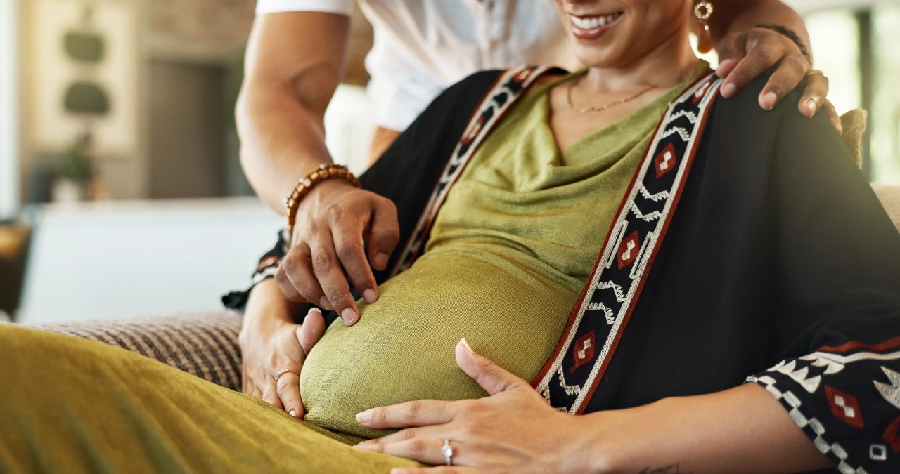 Smiling pregnant woman with her partner touching her baby bump, symbolizing hope, fertility, and pregnancy possibilities after menopause in India.