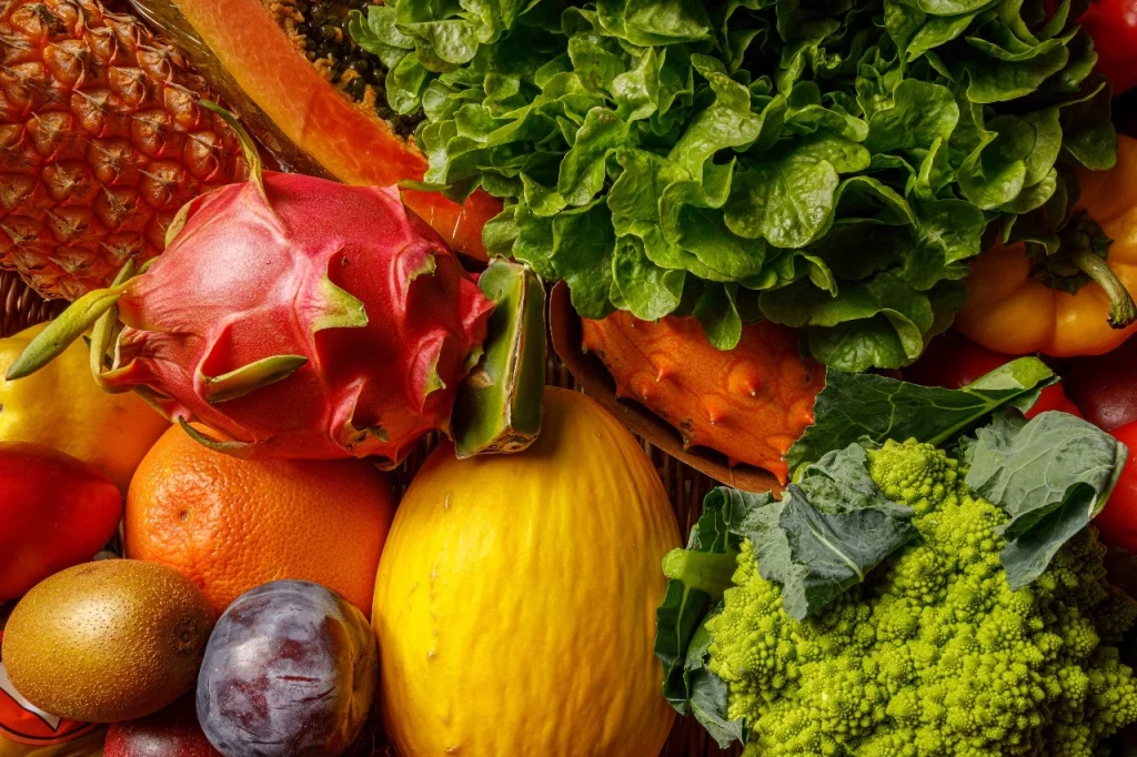 A colorful assortment of fresh tropical fruits and leafy greens including dragon fruit, papaya, pineapple, kale, and lettuce, symbolizing natural detox and nourishment.