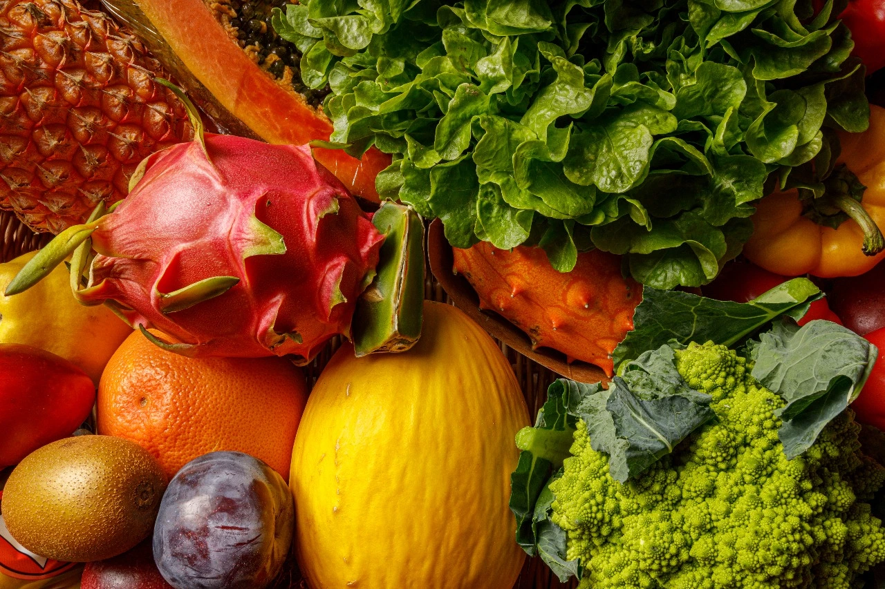A colorful assortment of fresh tropical fruits and leafy greens including dragon fruit, papaya, pineapple, kale, and lettuce, symbolizing natural detox and nourishment.
