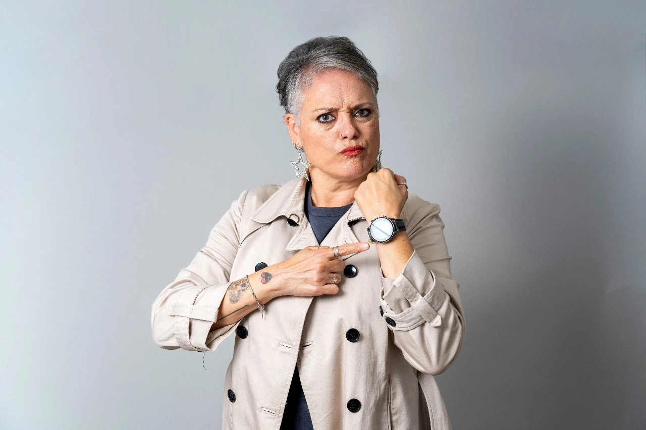 Confident mature woman pointing at her wristwatch, symbolizing time awareness and empowerment during menopause and aging gracefully.
