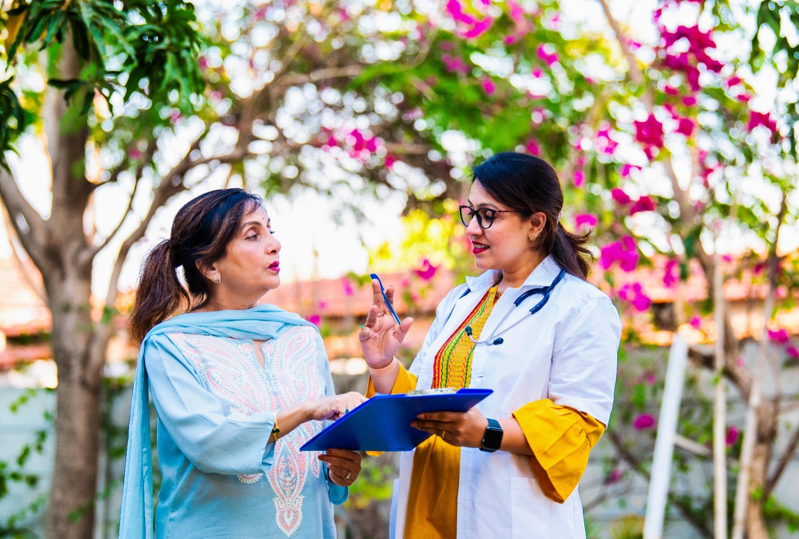 Female doctor discussing menopause symptoms and wellness care with an Indian woman in her 40s during a health consultation in a garden setting