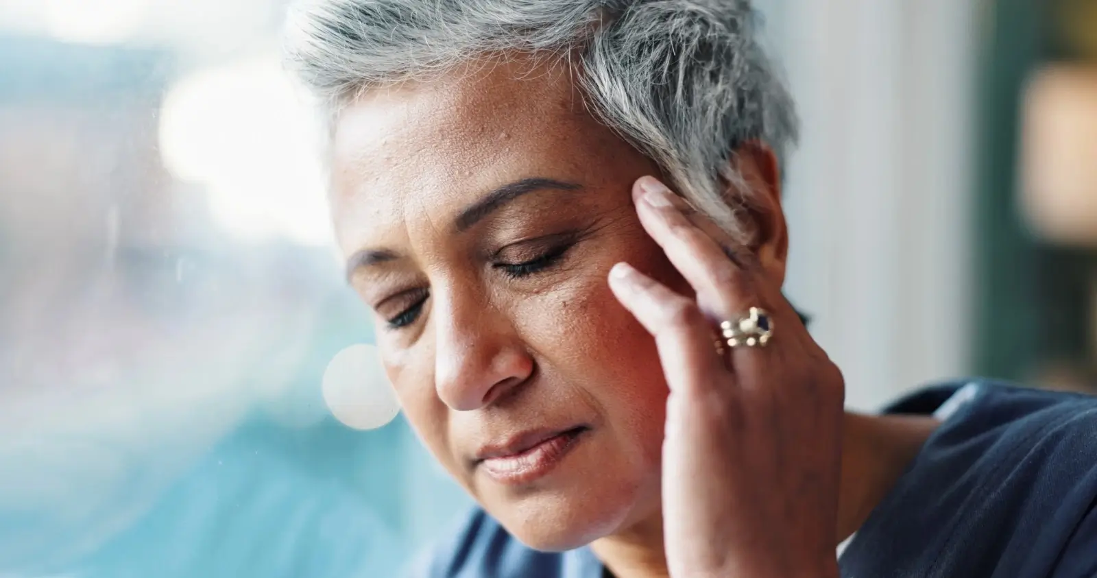 Middle-aged woman with grey hair experiencing headache and fatigue, a common menopause symptom.
