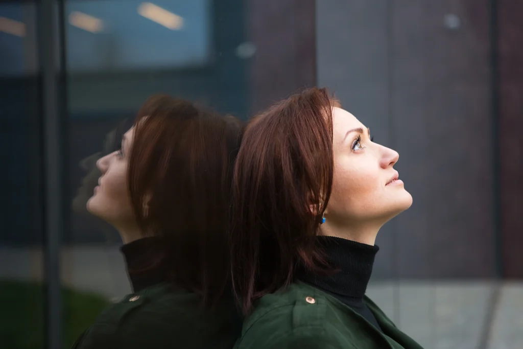 A thoughtful woman standing by a window with a calm reflective expression, symbolising awareness of hormonal changes and the estrogen effects on the body and mind.
