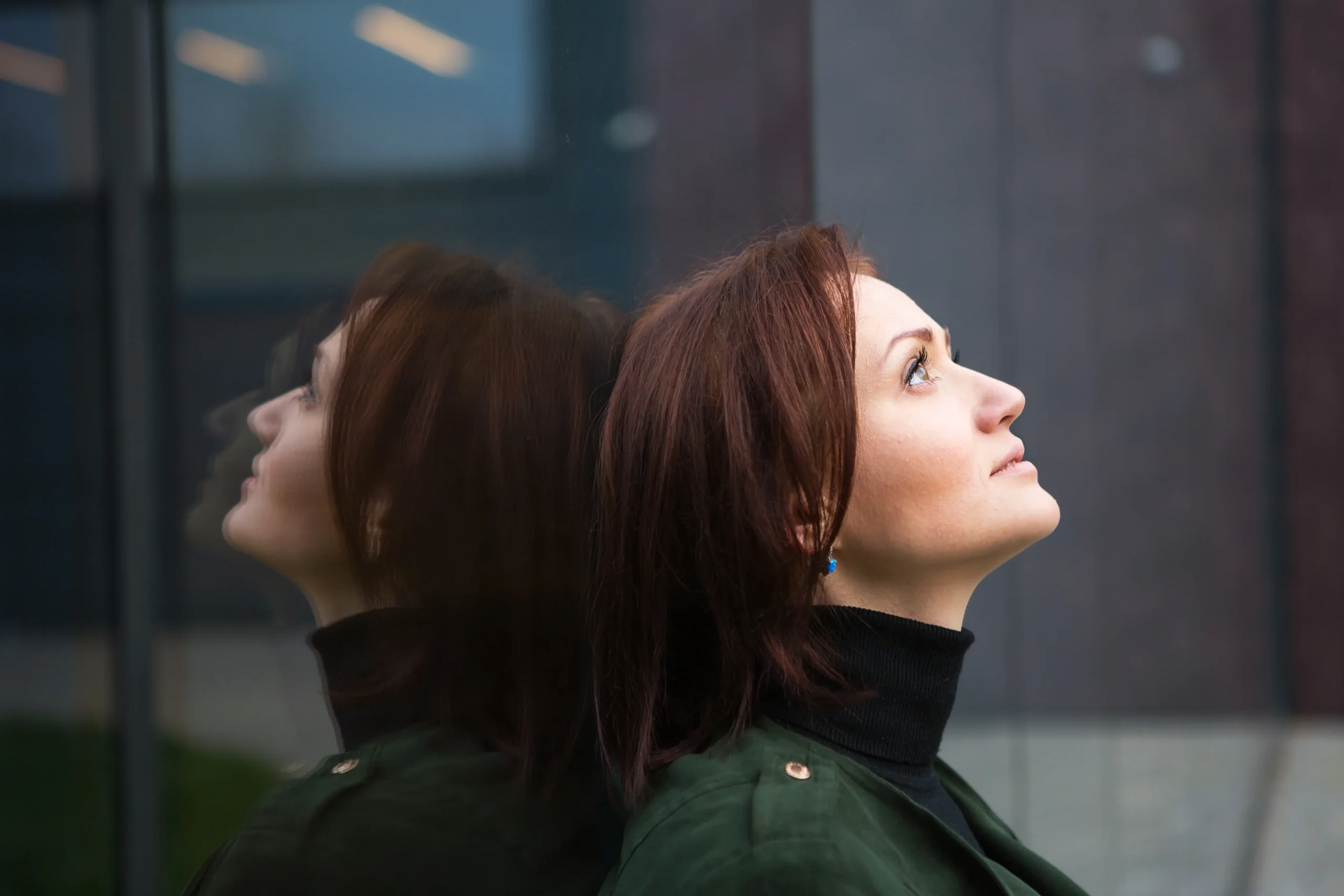 A thoughtful woman standing by a window with a calm reflective expression, symbolising awareness of hormonal changes and the estrogen effects on the body and mind.