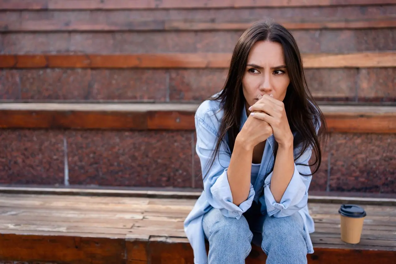 A worried woman sitting on outdoor steps, reflecting signs commonly misdiagnosed during perimenopause.