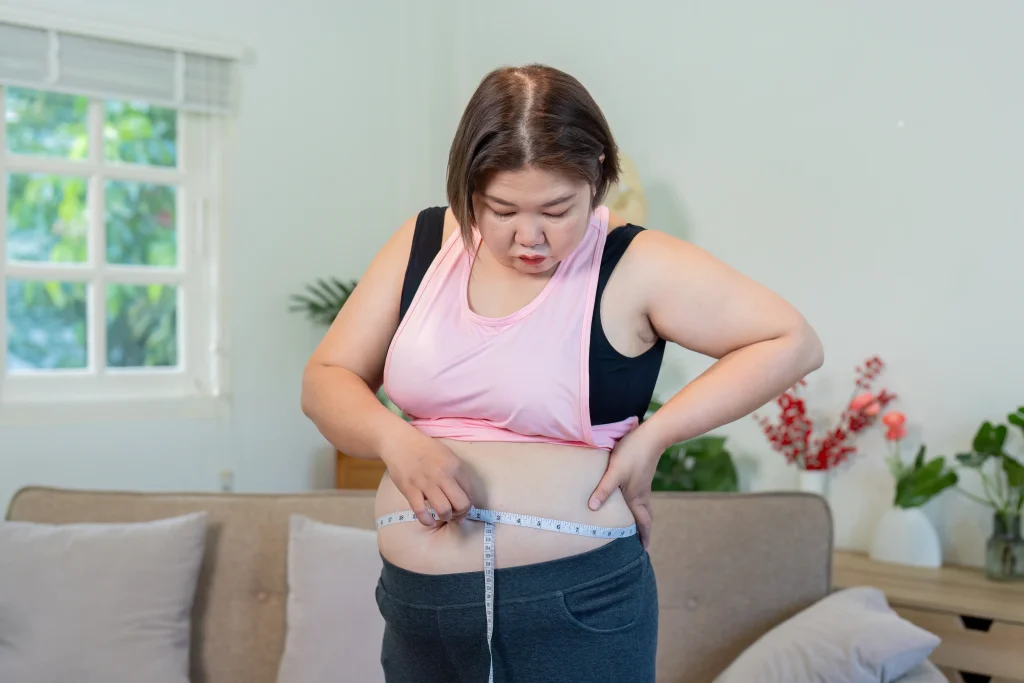A woman measuring her waistline at home, assessing midsection weight changes commonly experienced during menopause.