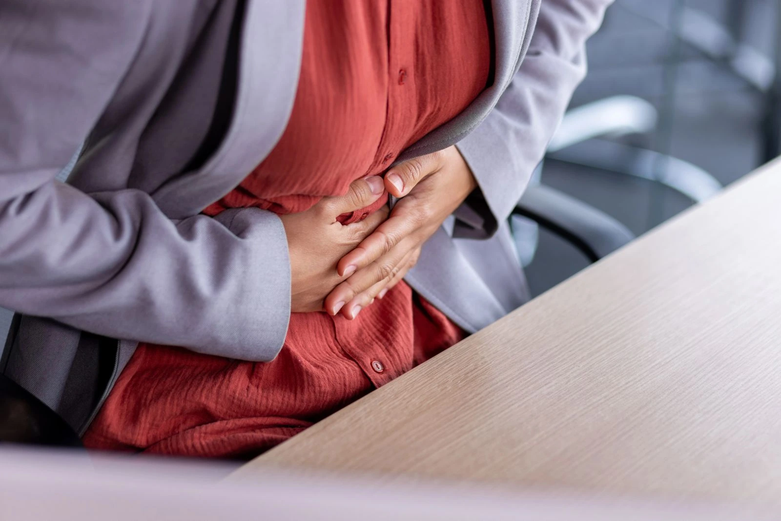Working woman experiencing IBS symptoms, holding her abdomen due to bloating and abdominal pain during work hours
