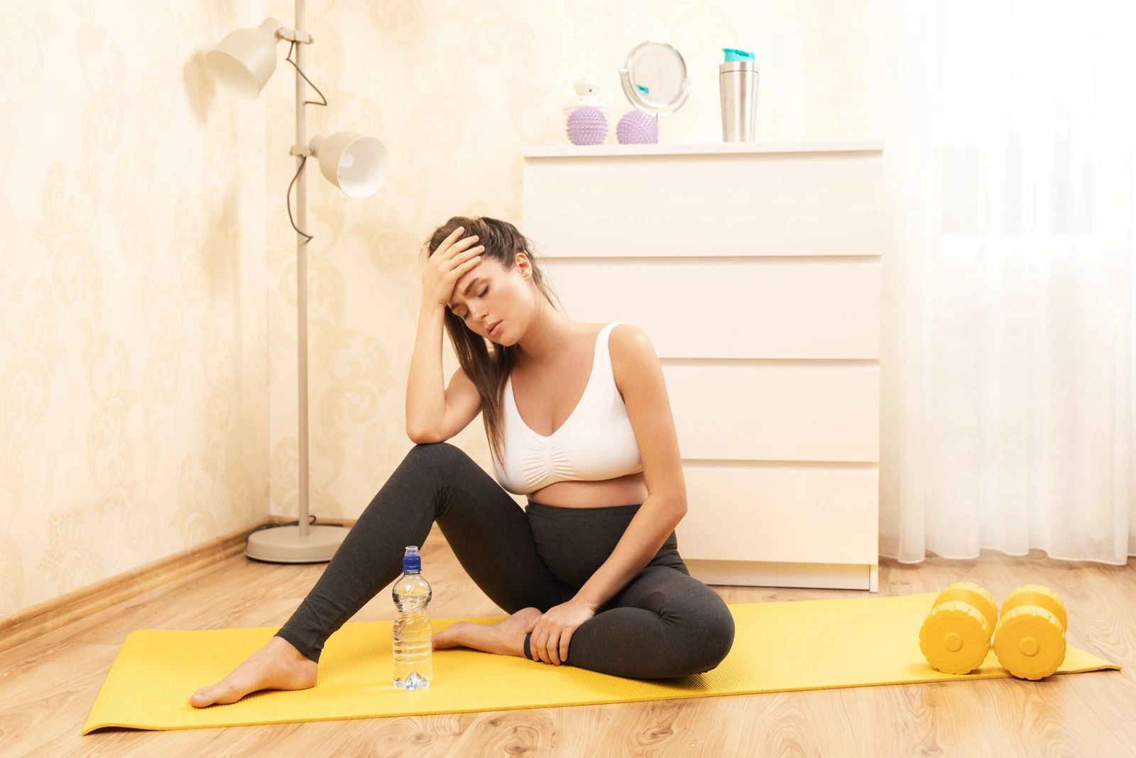 Woman in her 30s sitting on a yoga mat looking fatigued after exercise, representing stress, cortisol imbalance, sleep disruption and weight gain after 30.
