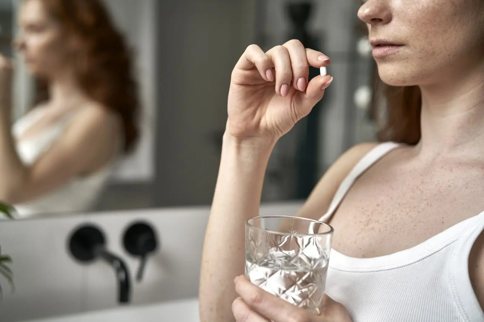 Woman holding a glass of water and an estrogen supplement pill, representing hormone support and menopause symptom management.