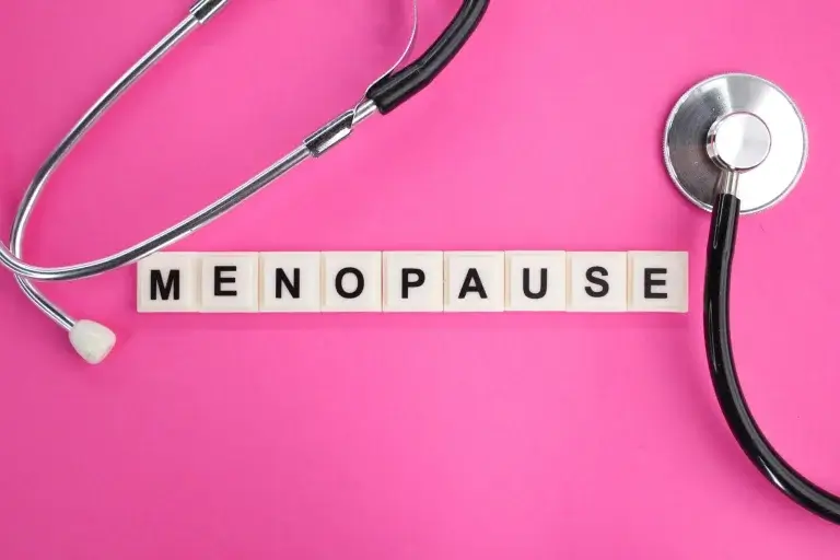 Stethoscope and letter blocks spelling menopause on a pink background representing medical tests and signs used to confirm menopause in women