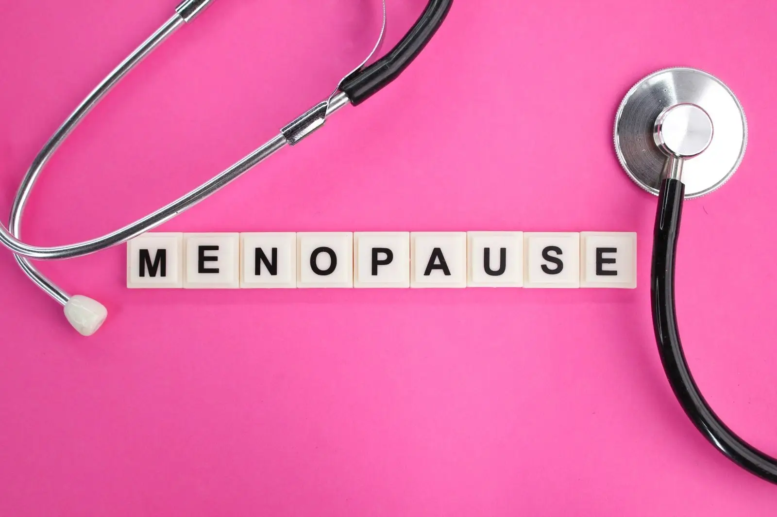 Stethoscope and letter blocks spelling menopause on a pink background representing medical tests and signs used to confirm menopause in women