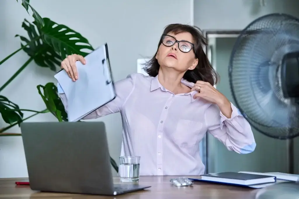Midlife woman experiencing menopause hot flash symptoms at work, feeling sudden heat, sweating, and discomfort during hormonal changes