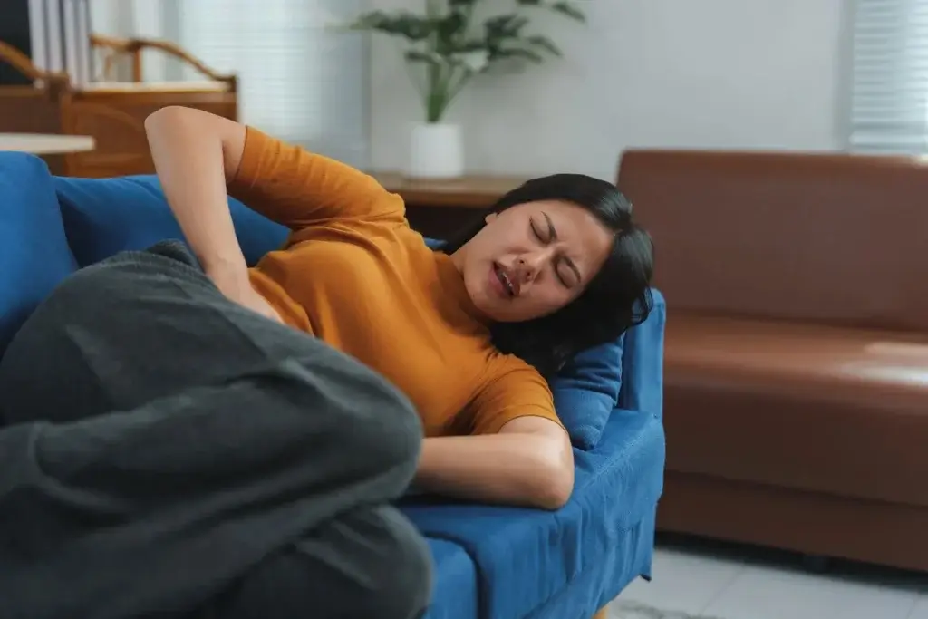 Woman experiencing severe perimenopausal bleeding symptoms, lying on sofa with abdominal pain and hormonal imbalance signs