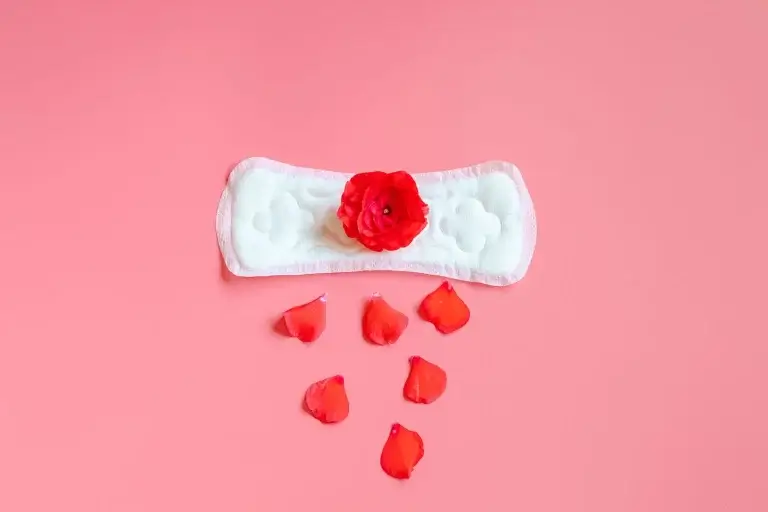 Perimenopause spotting represented by a sanitary pad with rose petals on a pink background, symbolising irregular bleeding and hormonal changes in midlife women.