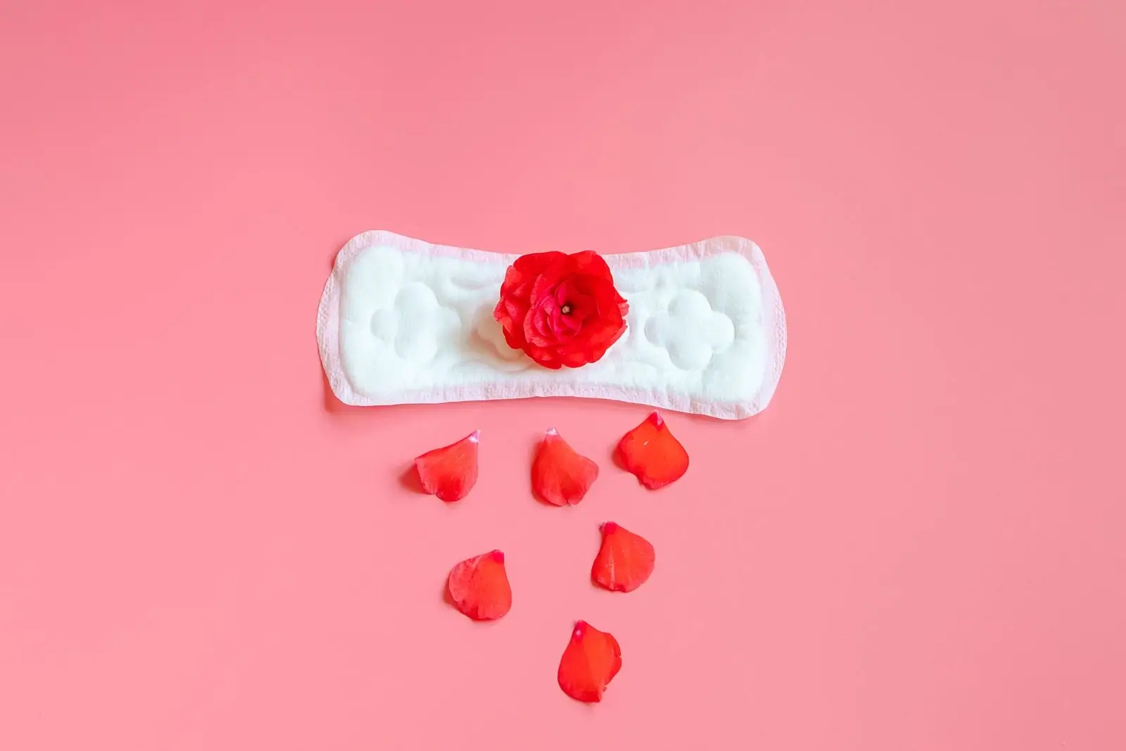 Perimenopause spotting represented by a sanitary pad with rose petals on a pink background, symbolising irregular bleeding and hormonal changes in midlife women.