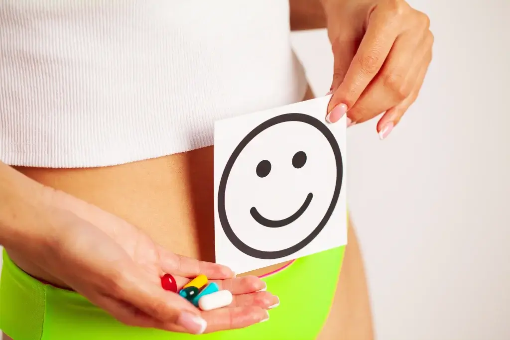 Progesterone tablets and hormonal balance concept with woman holding smiley card over abdomen symbolising mood stability and reproductive health