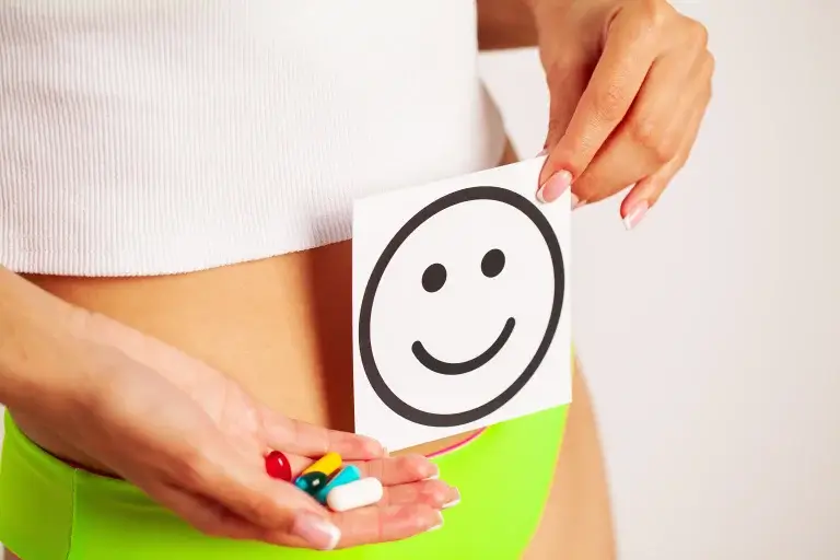 Progesterone tablets and hormonal balance concept with woman holding smiley card over abdomen symbolising mood stability and reproductive health