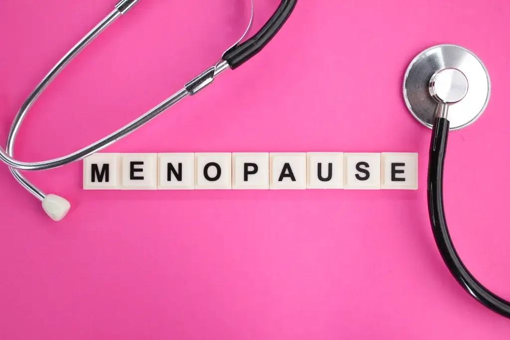 Menopause awareness concept with stethoscope and letter tiles spelling “menopause” on a pink background, representing women’s health, hormonal changes, and midlife wellness