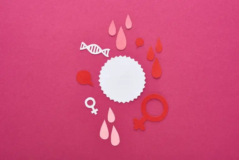Paper-cut illustration of menopause sex drive concept with female symbols, blood drops, and DNA elements around a blank label on a pink background.