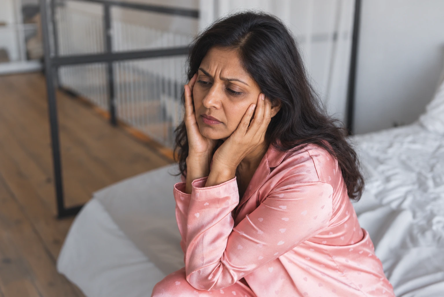 Indian woman experiencing hormonal anxiety during perimenopause while sitting awake in bed.